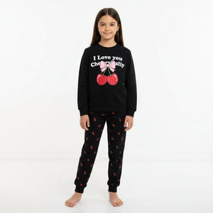 Young girl wearing a black pajama set with cherry and bow design in a room.