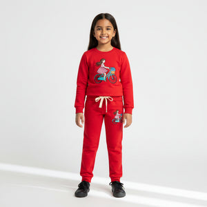 A young girl modeling a red two-piece sweatshirt and jogger pants set with embroidered cartoon bicycle designs, set against a plain white studio background.