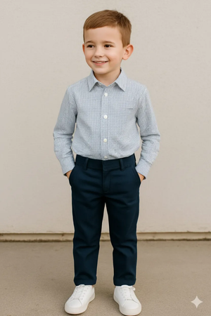 Boy smiling in a silver and black dots full sleeve casual shirt, navy pants, and white sneakers against a neutral background.