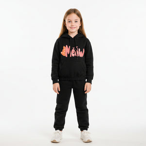Young girl wearing a black hoodie with colorful text in a living room.