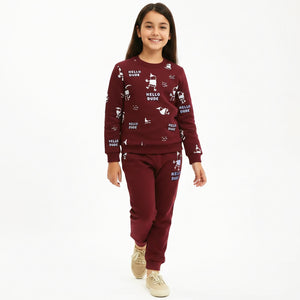 A young girl modeling a matching burgundy sweatshirt and jogger pants set with white cartoon graphics and 'HELLO DUDE' text, paired with beige sneakers, against a plain white background.
