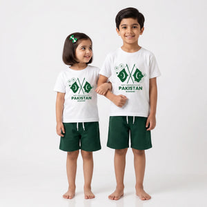 A young boy and girl standing side by side in matching white t-shirts and dark green shorts. Both shirts feature a green and white Pakistan flag graphic with the word 'PAKISTAN' printed below.