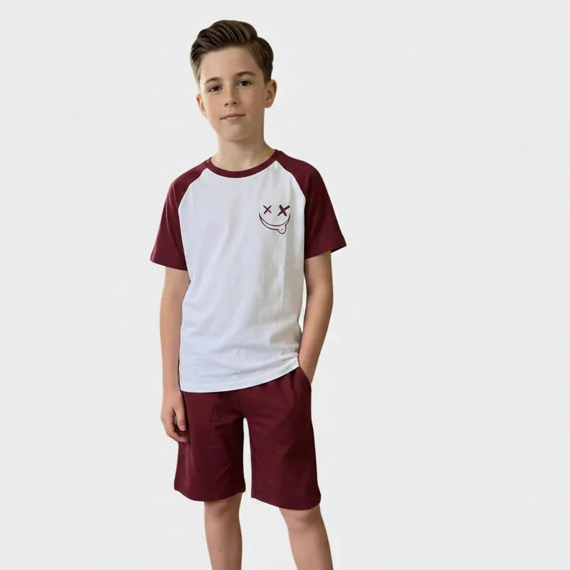 Young boy standing in a home setting wearing a white and maroon shirt with maroon shorts.