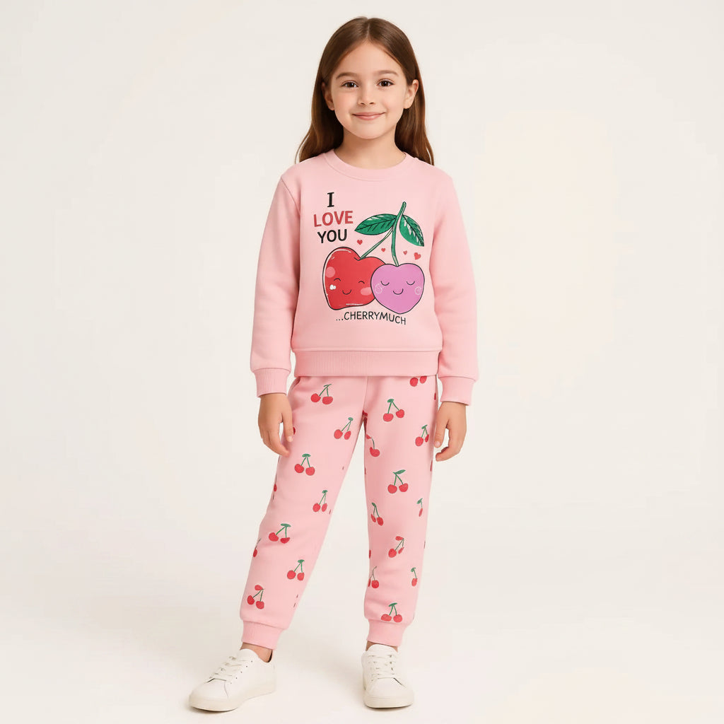 A young girl modeling a pink two-piece sweatshirt and jogger set with a cherry graphic on the sweatshirt and a cherry print on the pants, set against a plain light background.