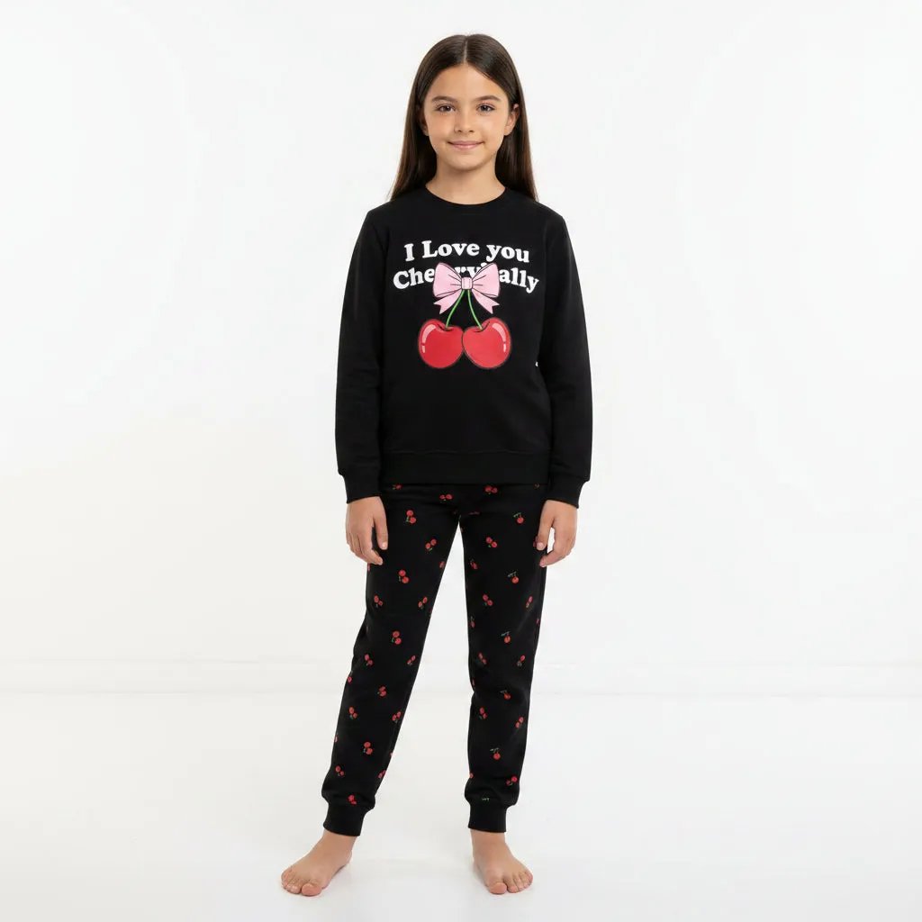 Young girl wearing a black pajama set with cherry and bow design in a room.