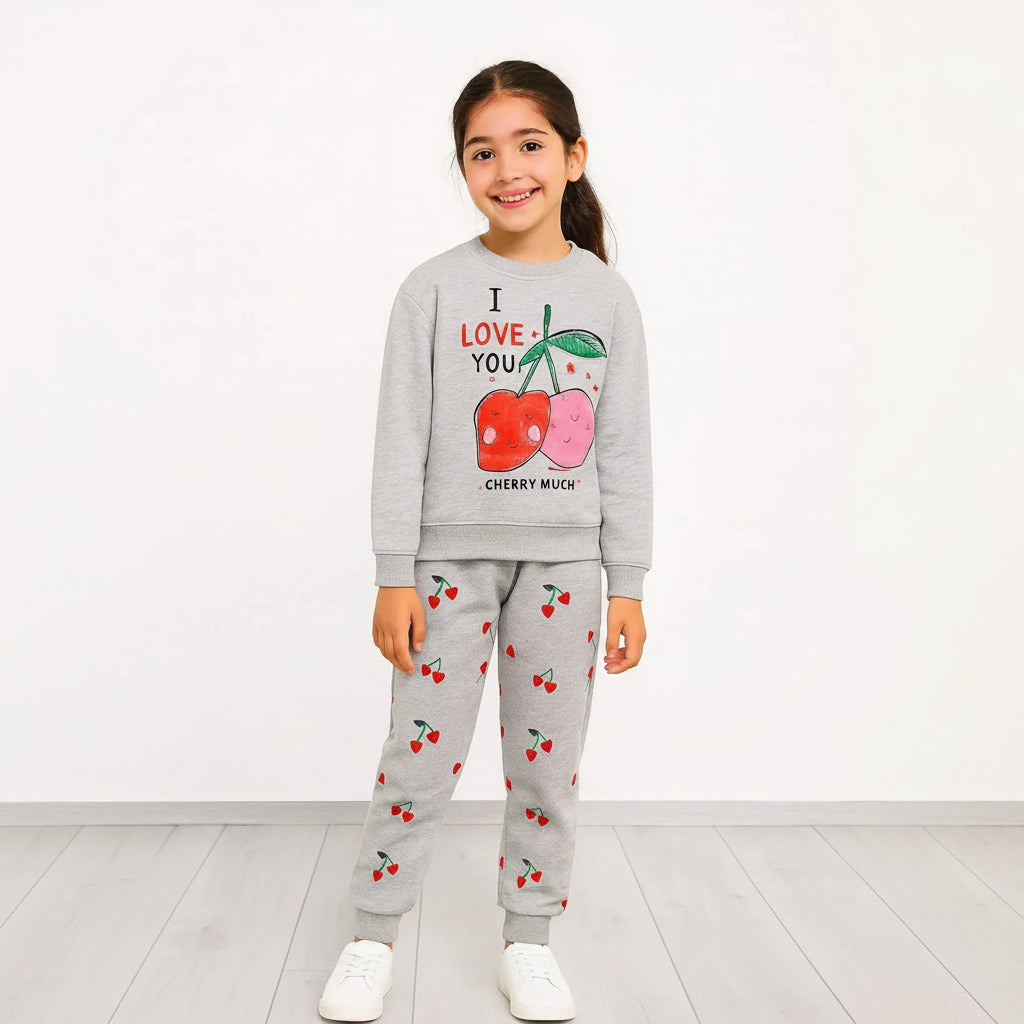 A young girl stands against a white wall wearing a light gray two-piece sweatshirt and jogger set. The sweatshirt features a graphic of two cherries with the text 'I LOVE YOU' and 'CHERRY MUCK'.
