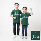 Two children modeling matching dark green t-shirts with white Arabic text and a crescent moon graphic, standing against a light gray studio background. A small inset in the bottom right shows a close-up of the shirt design.