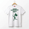 A white short-sleeve t-shirt hanging on a wooden hanger against a plain white background. The shirt features a green graphic print that reads 'HAPPY INDEPENDENCE DAY' above a silhouette of a runner carrying a Pakistan flag.