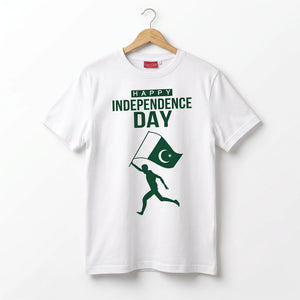 A white short-sleeve t-shirt hanging on a wooden hanger against a plain white background. The shirt features a green graphic print that reads 'HAPPY INDEPENDENCE DAY' above a silhouette of a runner carrying a Pakistan flag.