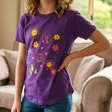 Young girl in a purple t-shirt with colorful designs standing in a living room.