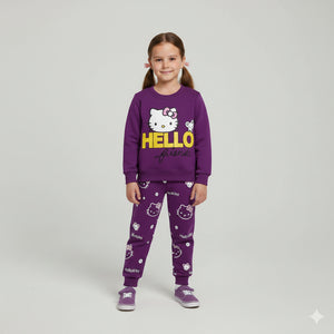 A young girl stands against a light gray studio background wearing a purple Hello Kitty pajama set with a sweatshirt and pants, along with matching purple shoes. The sweatshirt is purple with a large white Hello Kitty face and yellow 'HELLO' text on the front.