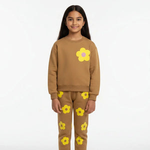 Young girl wearing a brown outfit with yellow flower patterns in a living room.