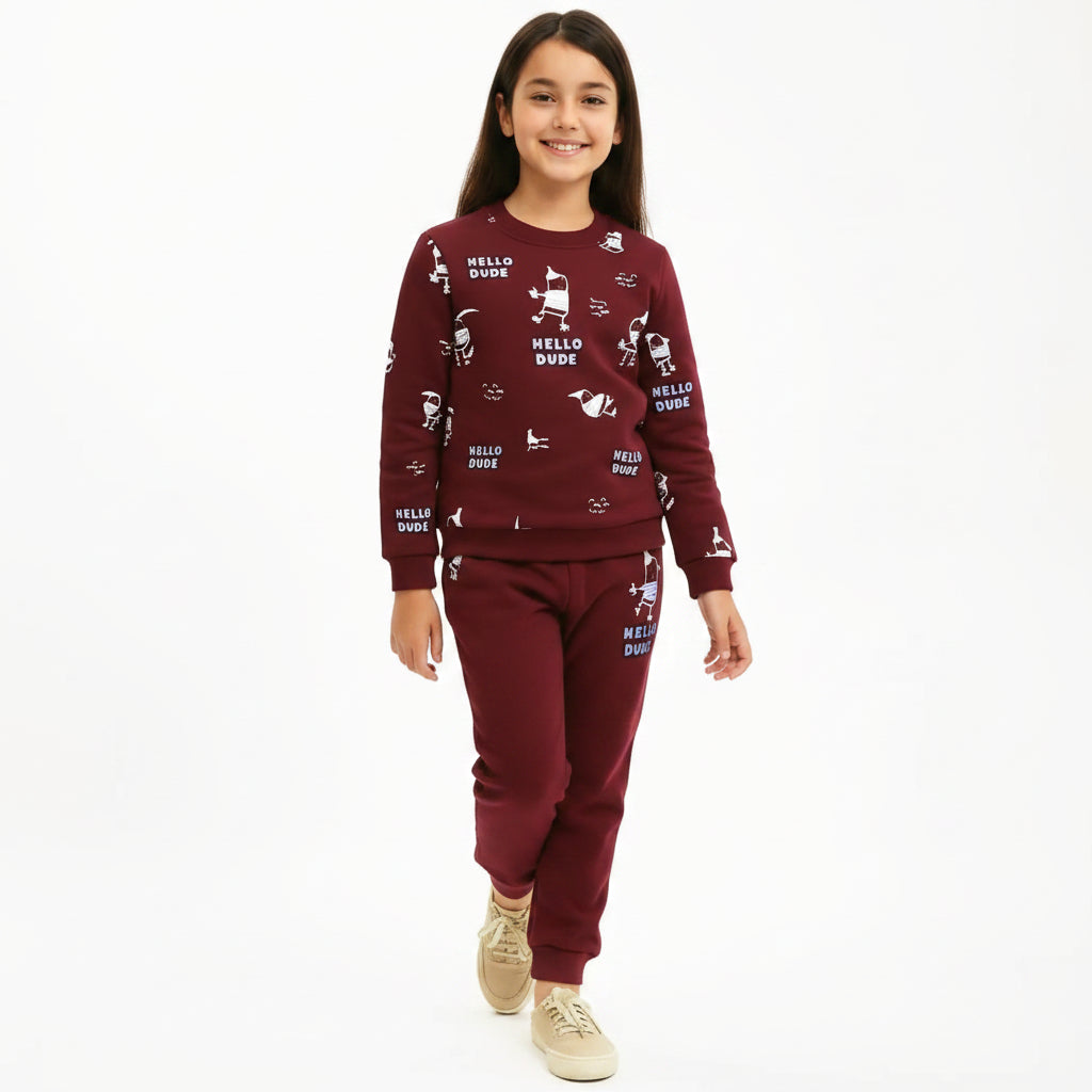 A young girl modeling a matching burgundy sweatshirt and jogger pants set with white cartoon graphics and 'HELLO DUDE' text, paired with beige sneakers, against a plain white background.
