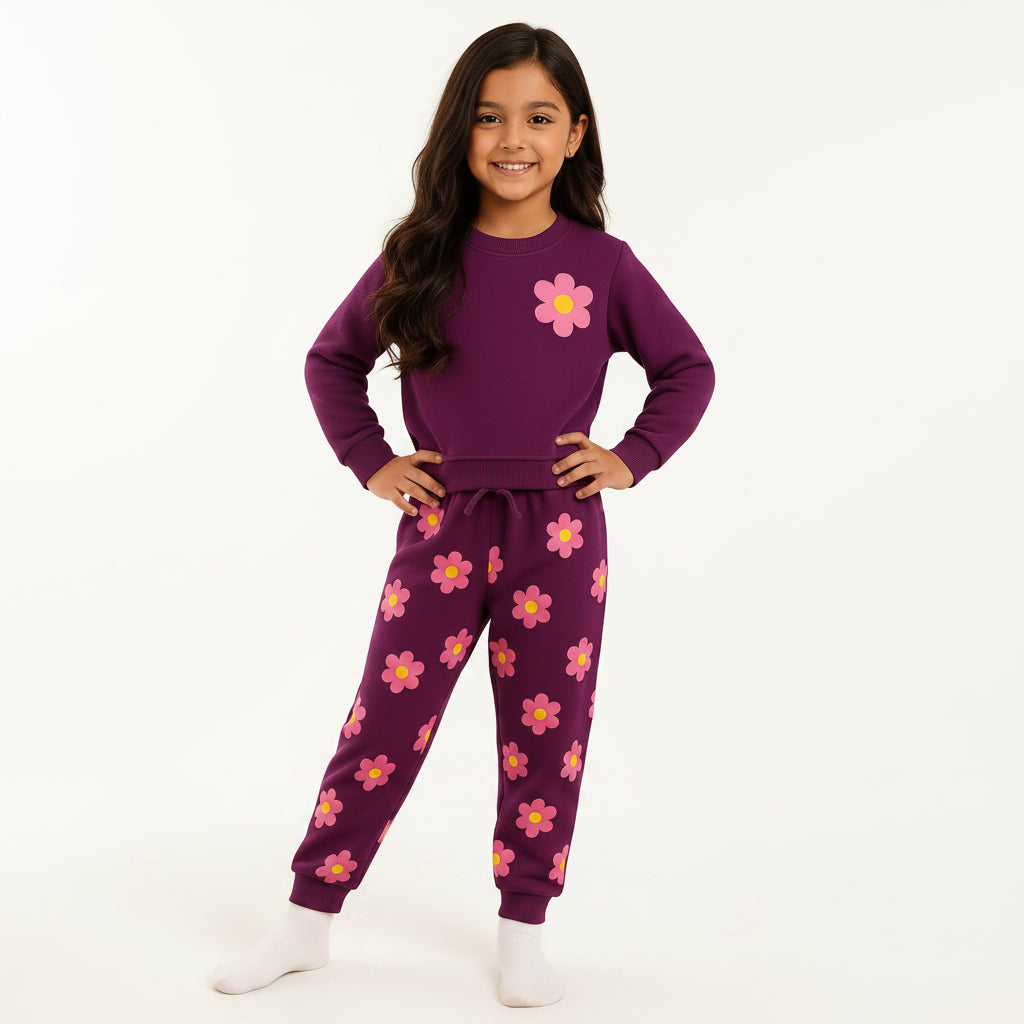 A young girl wearing a purple two-piece pajama set with pink and yellow flower prints, standing in a living room setting.